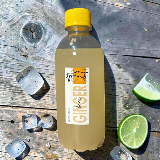 Die Spens Clarens homemade ginger beer in a clear plastic bottle with a yellow cap, served with ice and lime slices on a wooden surface.