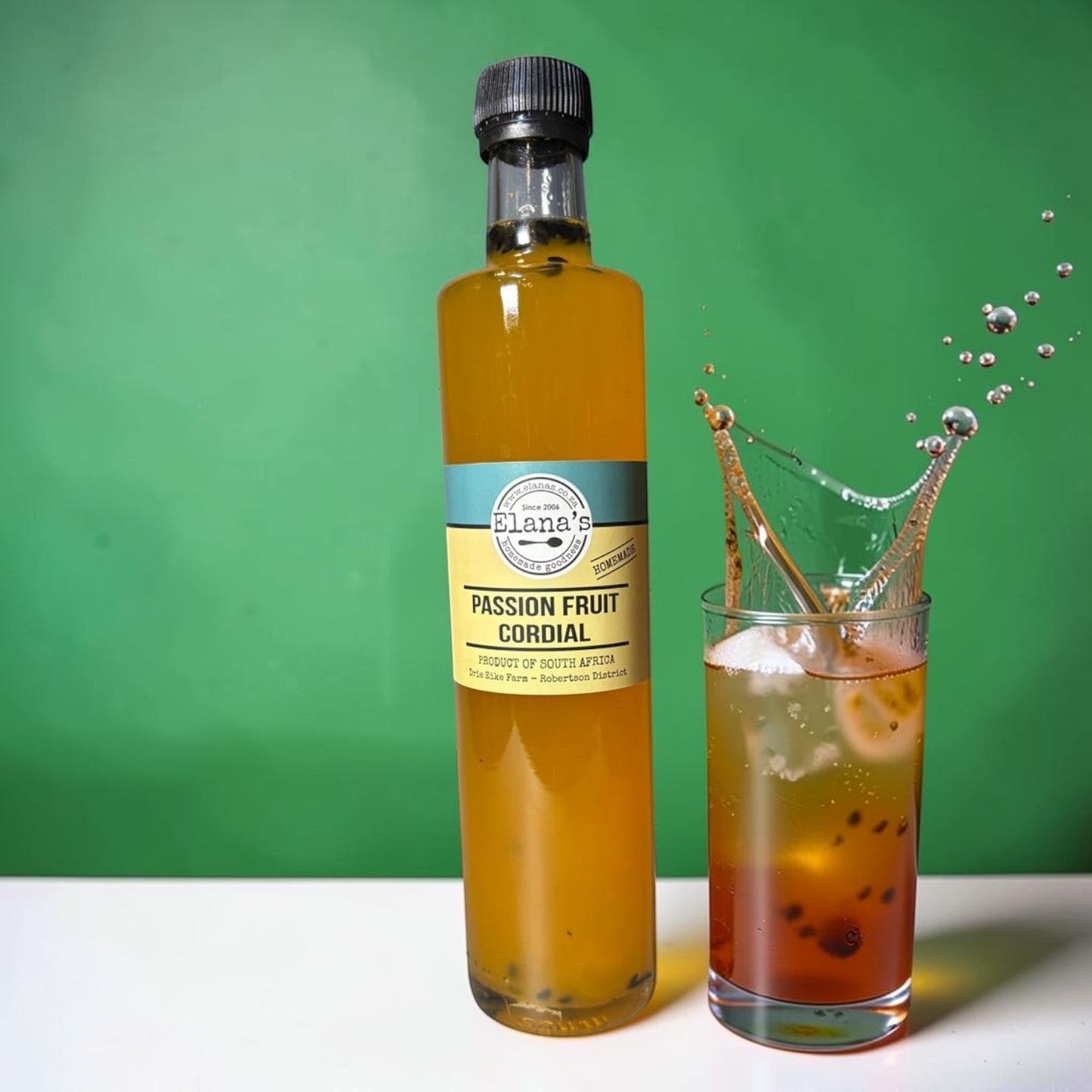 Die Spens Clarens Elanas Passion Fruit Cordial bottle next to a glass with a splash of cordial, ice, and passion fruit seeds.