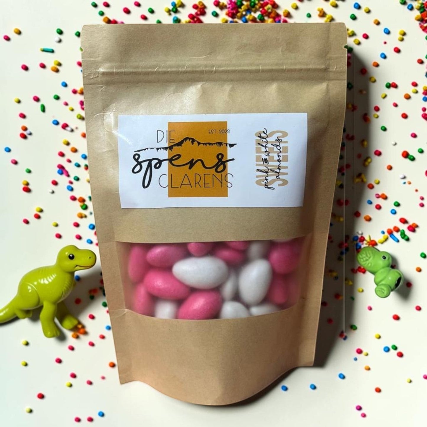 Die Spens Clarens pink and white candy-coated almonds in a resealable pouch, surrounded by sprinkles.