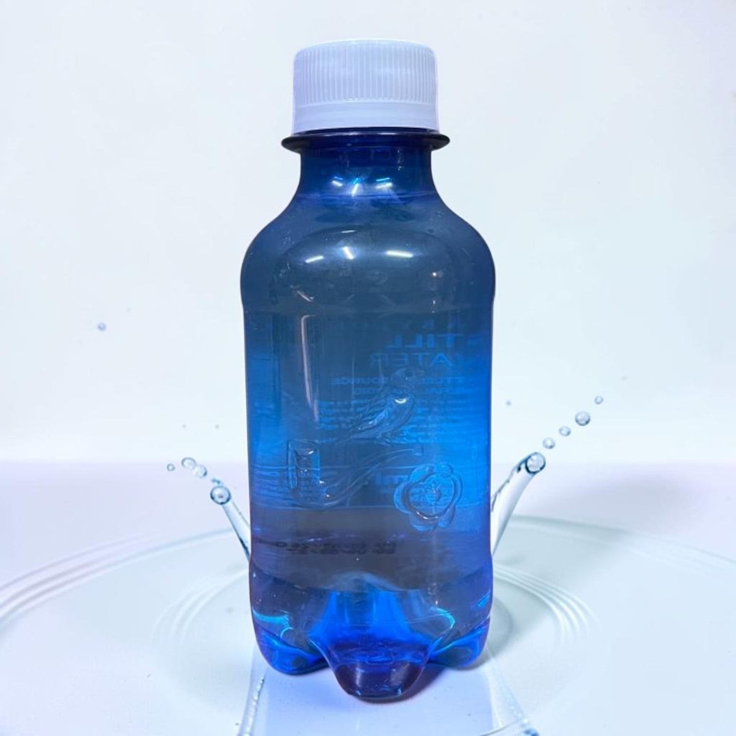 Die Spens Clarens 1L blue plastic bottle of still water with white cap, water splashes around the bottle.