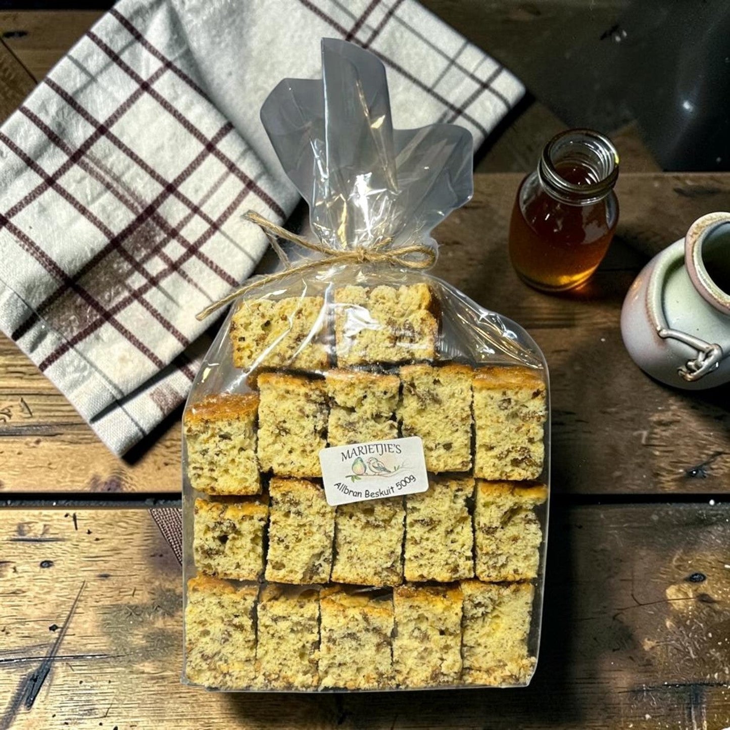 Die Spens Clarens Marietjies All Bran Beskuit, a package of 20 small, golden-brown, rectangular South African rusks with visible bran pieces, tied with twine.