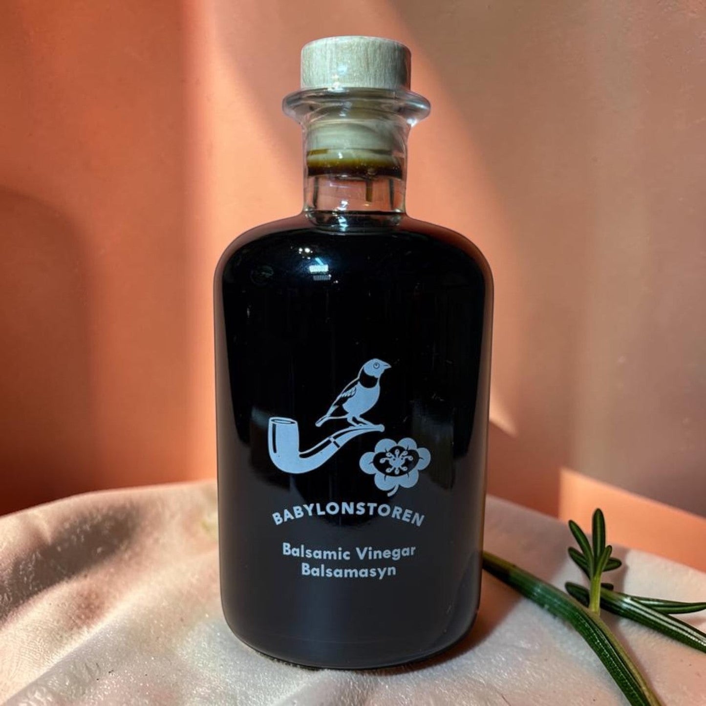 Die Spens Clarens Babylonstoren Balsamic Vinegar in a dark glass bottle with a wooden cork. Features a white bird on a pipe and flower graphic.