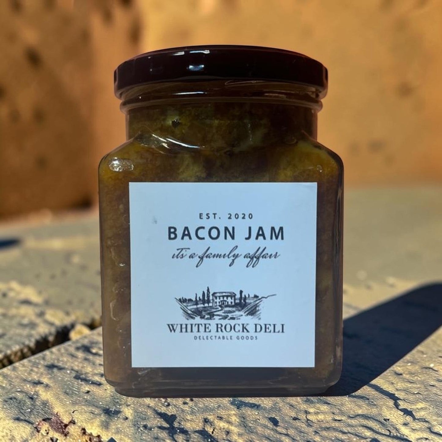 Die Spens Clarens White Rock Deli Bacon Jam in a glass jar with a dark lid. Savory condiment with smoky bacon and sweet notes.