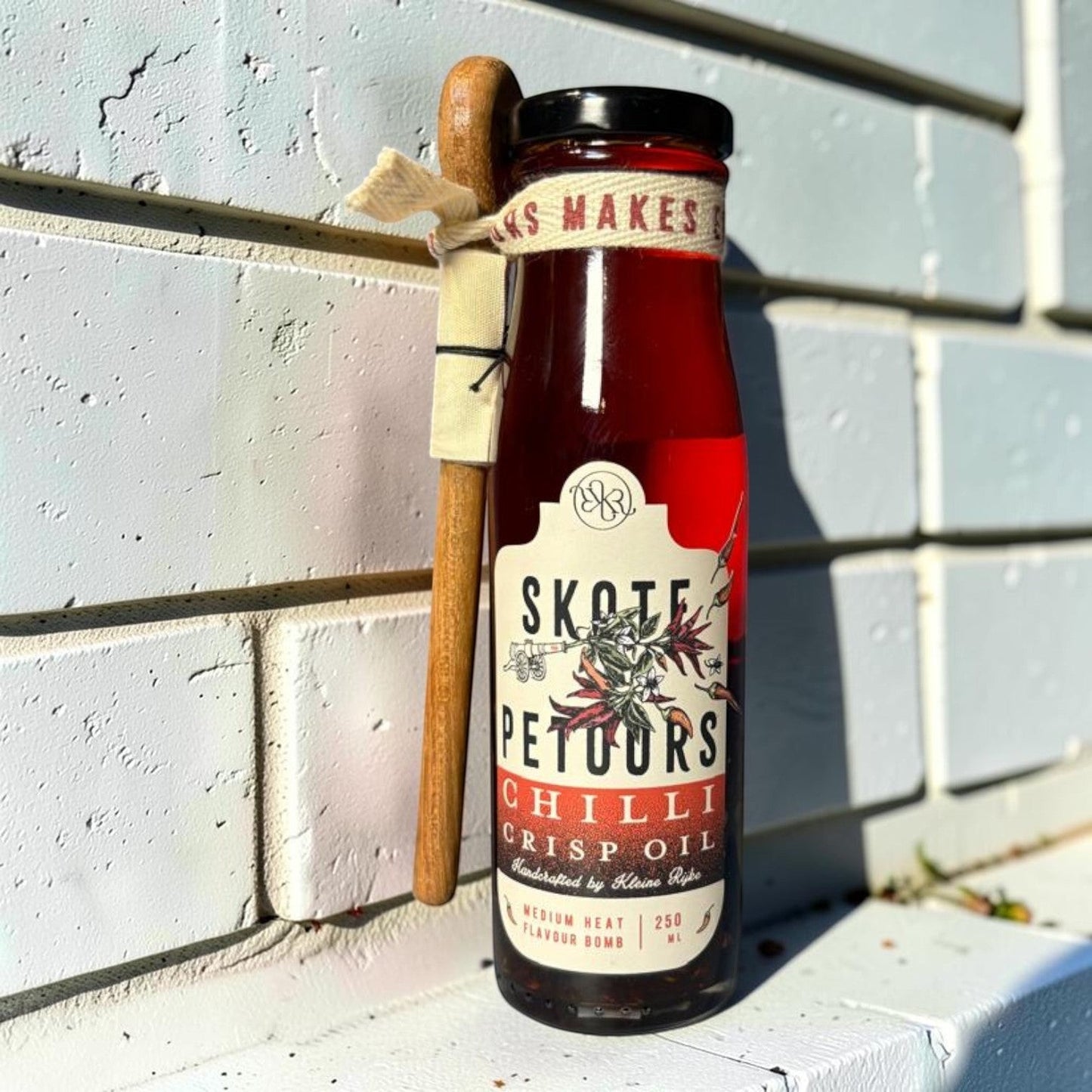 Die Spens Clarens Skote Petoors Chilli Crisp Oil in a glass bottle with a wooden spoon attached. Medium heat flavour bomb.