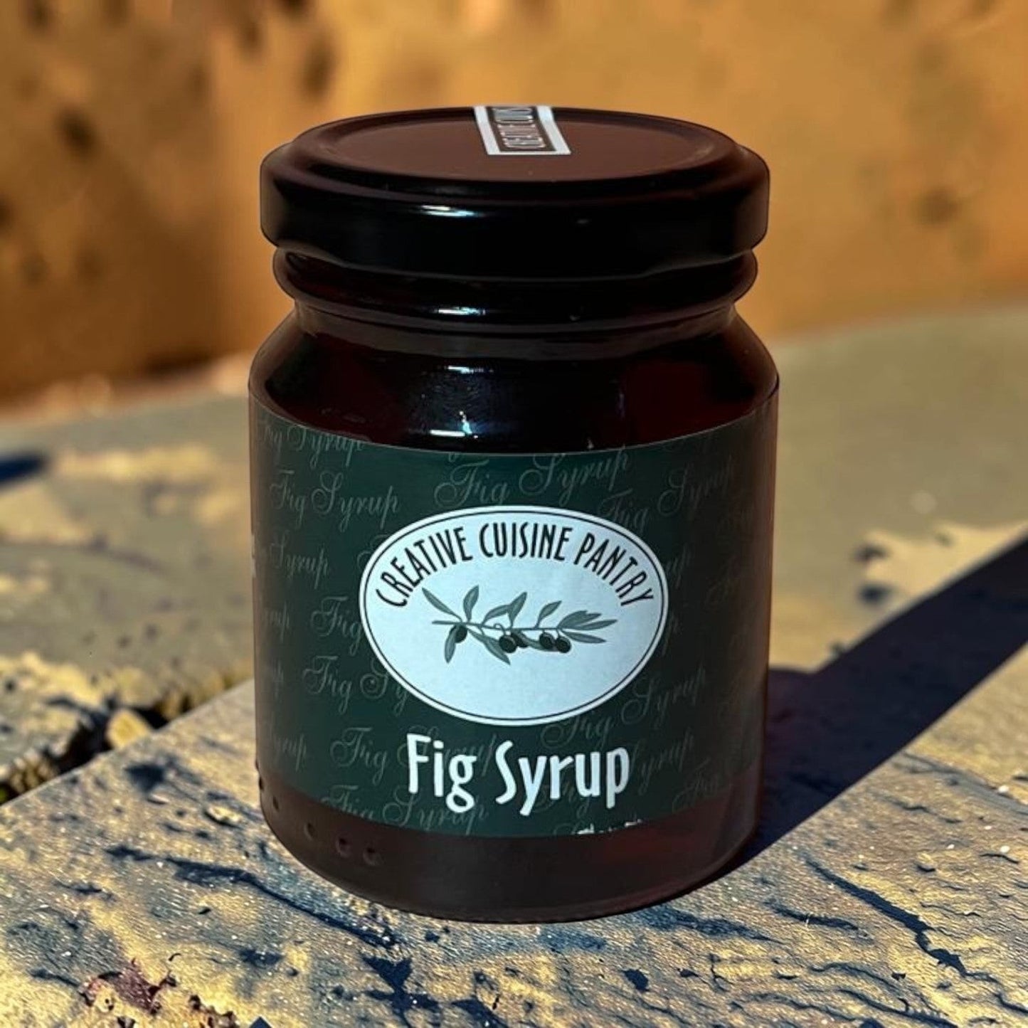 Die Spens Clarens Creative Cuisine Fig Syrup in a dark glass jar with a black lid, featuring a label with olive branches and text.