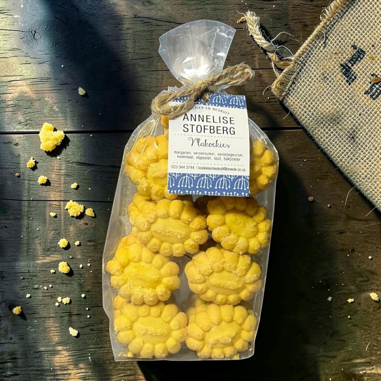 Die Spens Clarens Annelise Stofberg Vlakoekies, traditional South African butter cookies, golden yellow, crumbly texture, flower-shaped, packaged in a clear bag tied with twine.