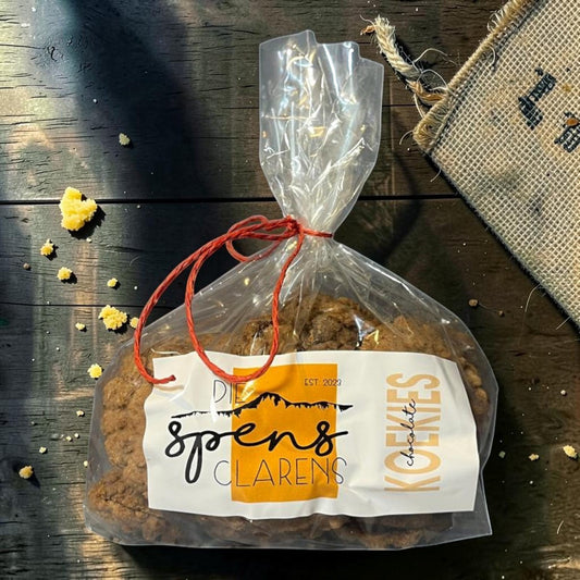 Die Spens Clarens chocolate koekies in a clear bag tied with red string, featuring large chocolate chunks and a rustic label.