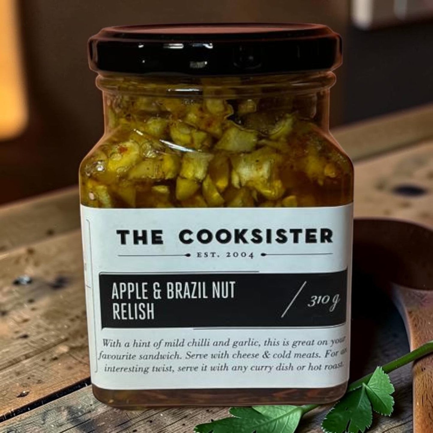 The Cooksister Apple & Brazil Nut Relish in a glass jar with a black lid. The relish contains chopped apples, Brazil nuts, chilli, and garlic.