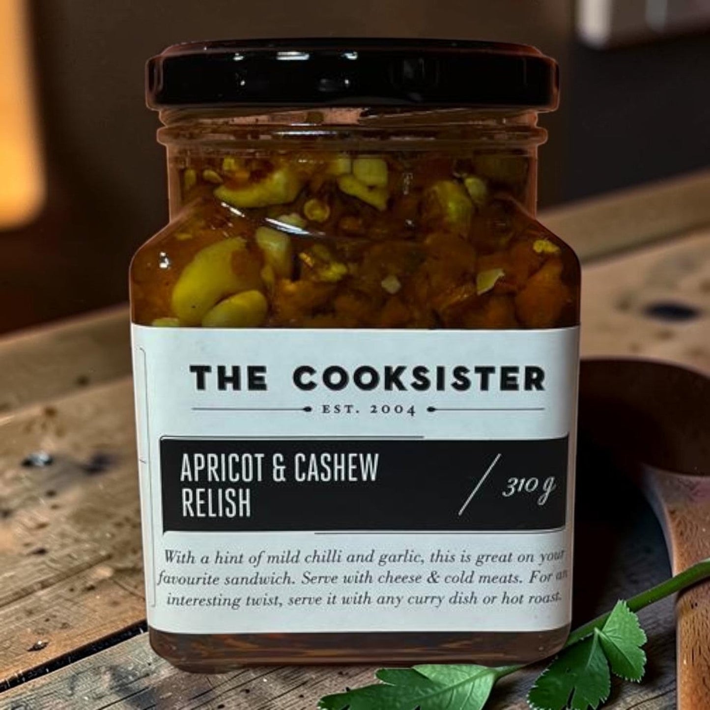The Cooksister Apricot & Cashew Relish in a glass jar with a black lid. Contains visible pieces of apricot and cashew nuts.