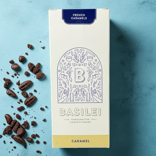 Die Spens Clarens Basilei French Caramels box with scattered chocolate pieces and coffee beans on a blue background.