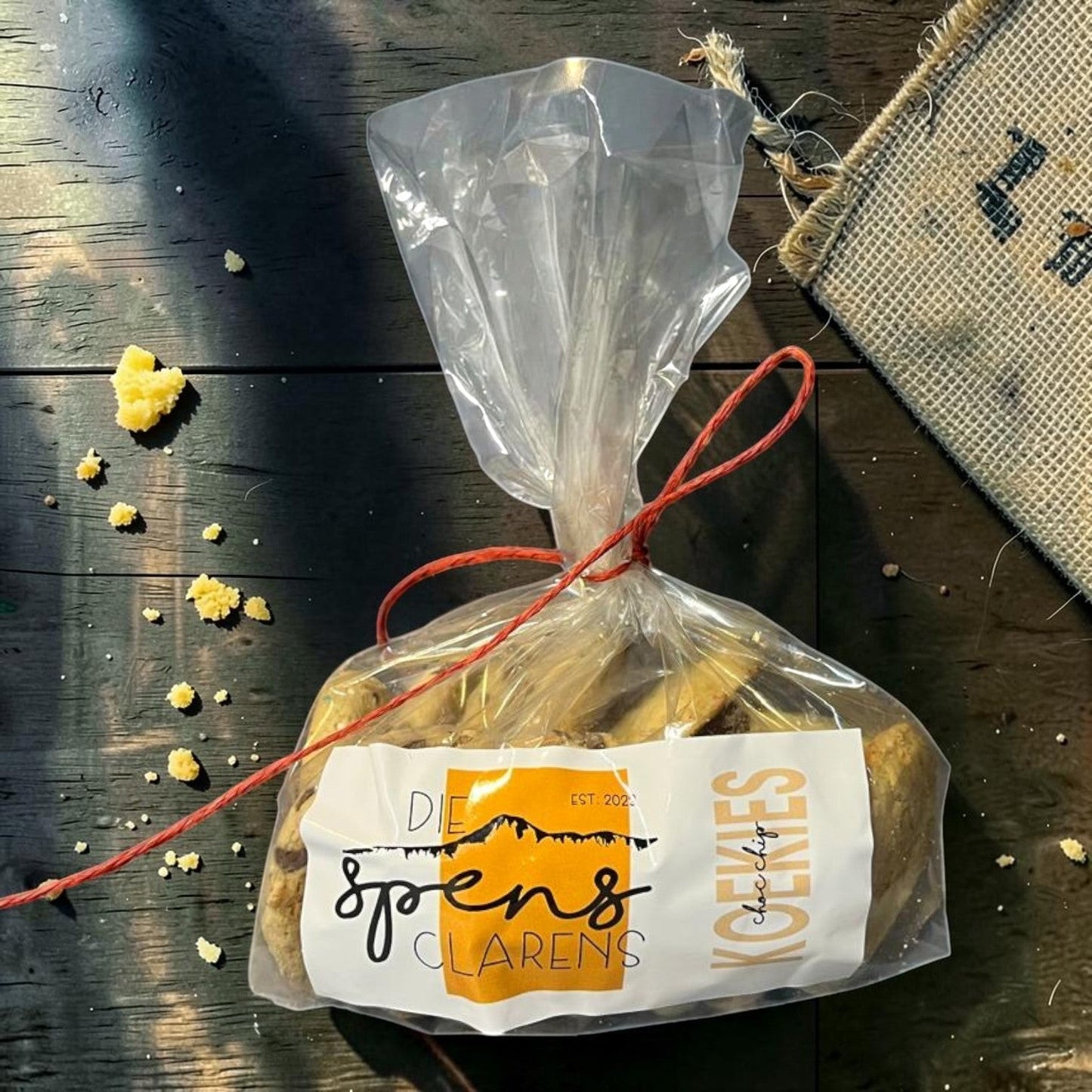 Die Spens Clarens large chocolate chip cookies in a clear plastic bag tied with red string, on a wooden surface.
