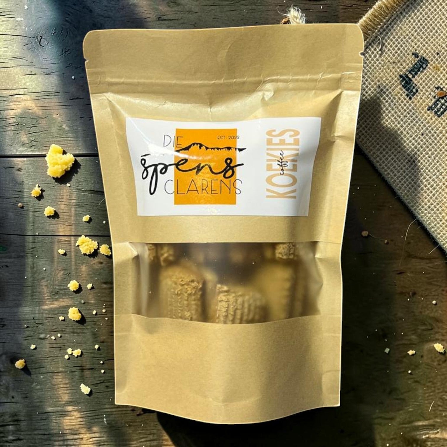 Die Spens Clarens small coffee biscuits in a resealable brown pouch, with crumbs scattered on a wooden surface.