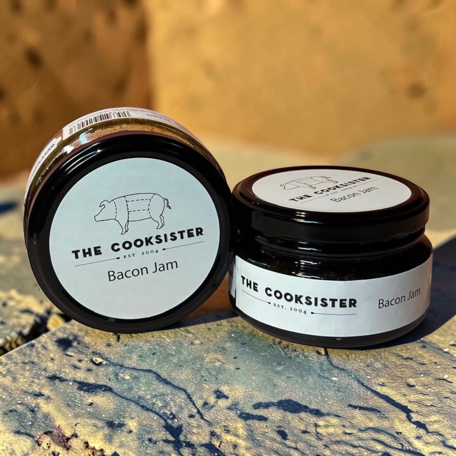 Die Spens Clarens Cooksister Bacon Jam in glass jars with black lids. Savory condiment for burgers and sandwiches.
