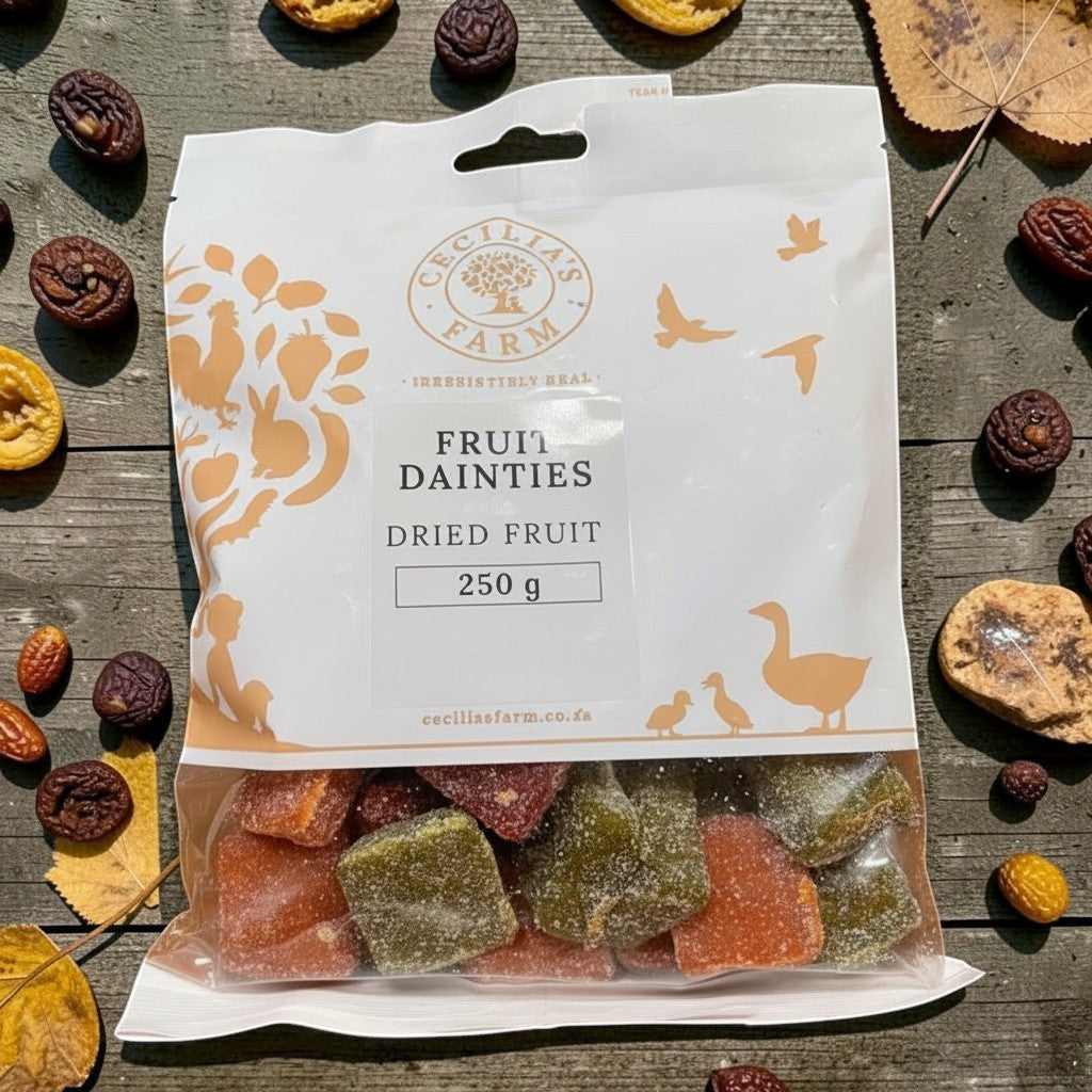 Die Spens Clarens Fruit Dainties dried fruit chews in orange and green, dusted with sugar. A 250g bag is shown on a wooden surface with scattered dried fruits and autumn leaves.