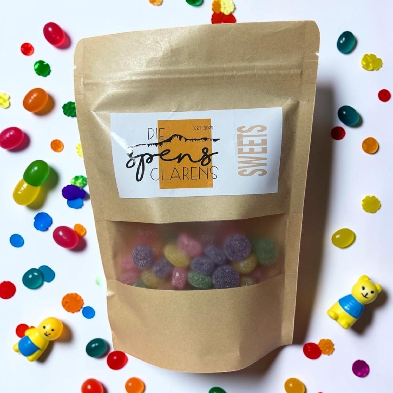 Die Spens Clarens assorted fruit jelly drops in a resealable pouch, surrounded by colorful candy pieces and small toys.