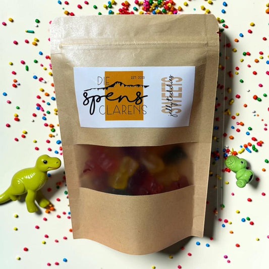 Die Spens Clarens resealable pouch of assorted color jelly teddies surrounded by colorful sprinkles and toy dinosaurs.