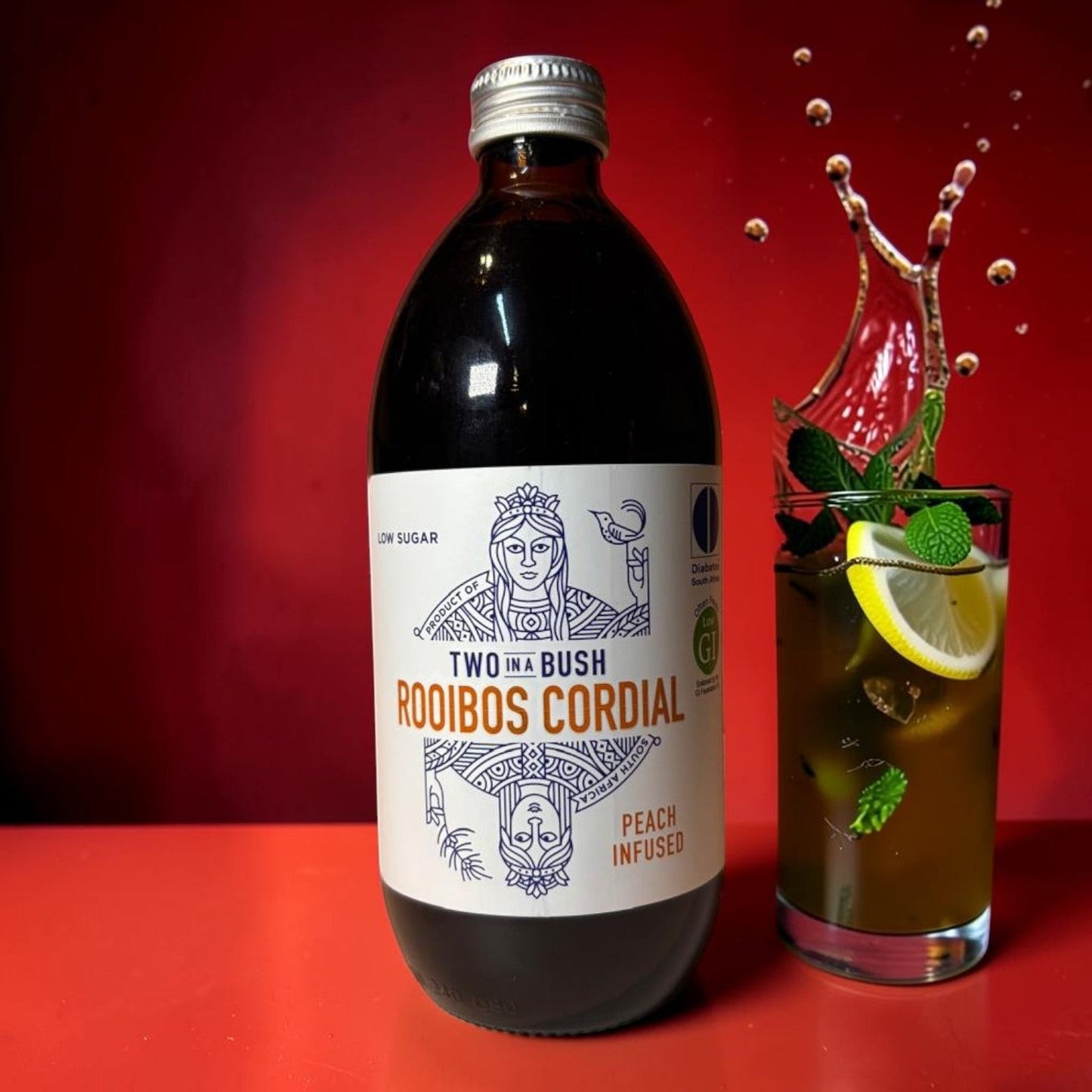 Die Spens Clarens Two In A Bush low sugar peach infused rooibos cordial bottle next to a refreshing drink with lemon and mint.