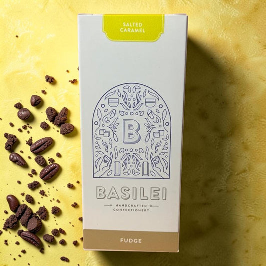 Die Spens Clarens Basilei Salted Caramel Fudge box with scattered fudge pieces and crumbs on a yellow textured background.