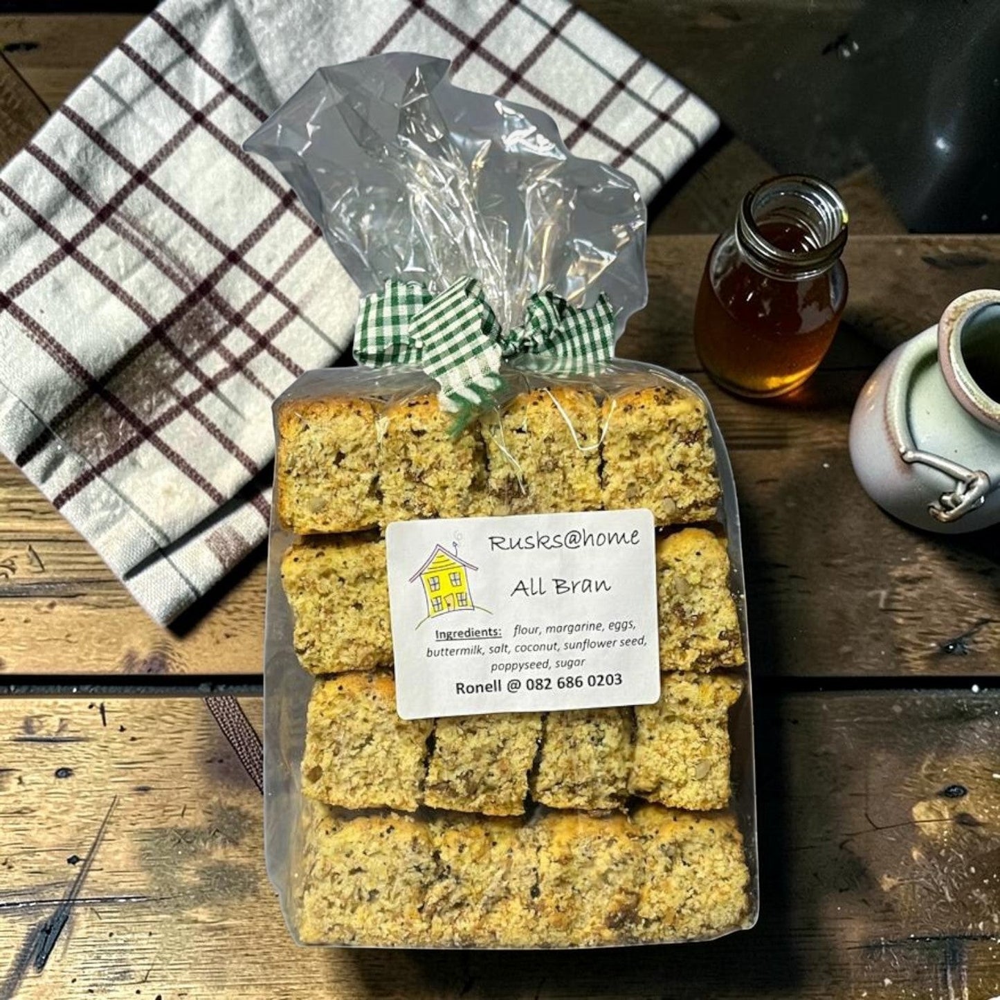 Die Spens Clarens All Bran rusks in a clear package, tied with a green gingham bow. Baked with flour, margarine, eggs, buttermilk, salt, coconut, sunflower seed, and poppyseed.