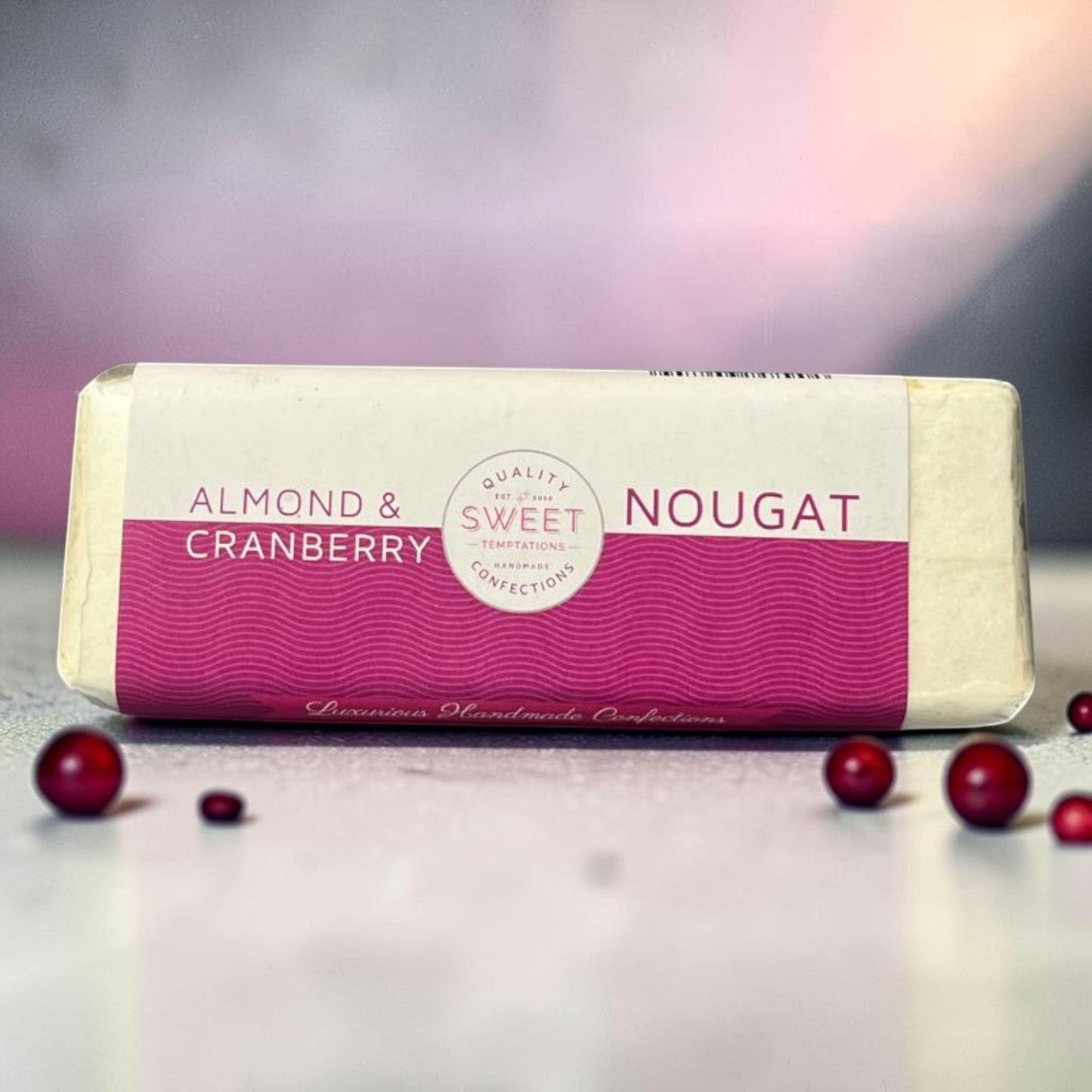 Die Spens Clarens Almond & Cranberry Nougat bar with a pink wavy pattern and text. Handmade confection with crunchy almonds and chewy cranberries.