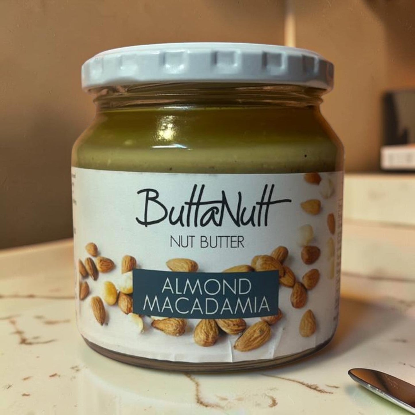 Die Spens Clarens ButtaNutt Almond Macadamia Nut Butter in a glass jar with a white lid. Smooth, creamy spread with whole almonds and macadamia nuts.