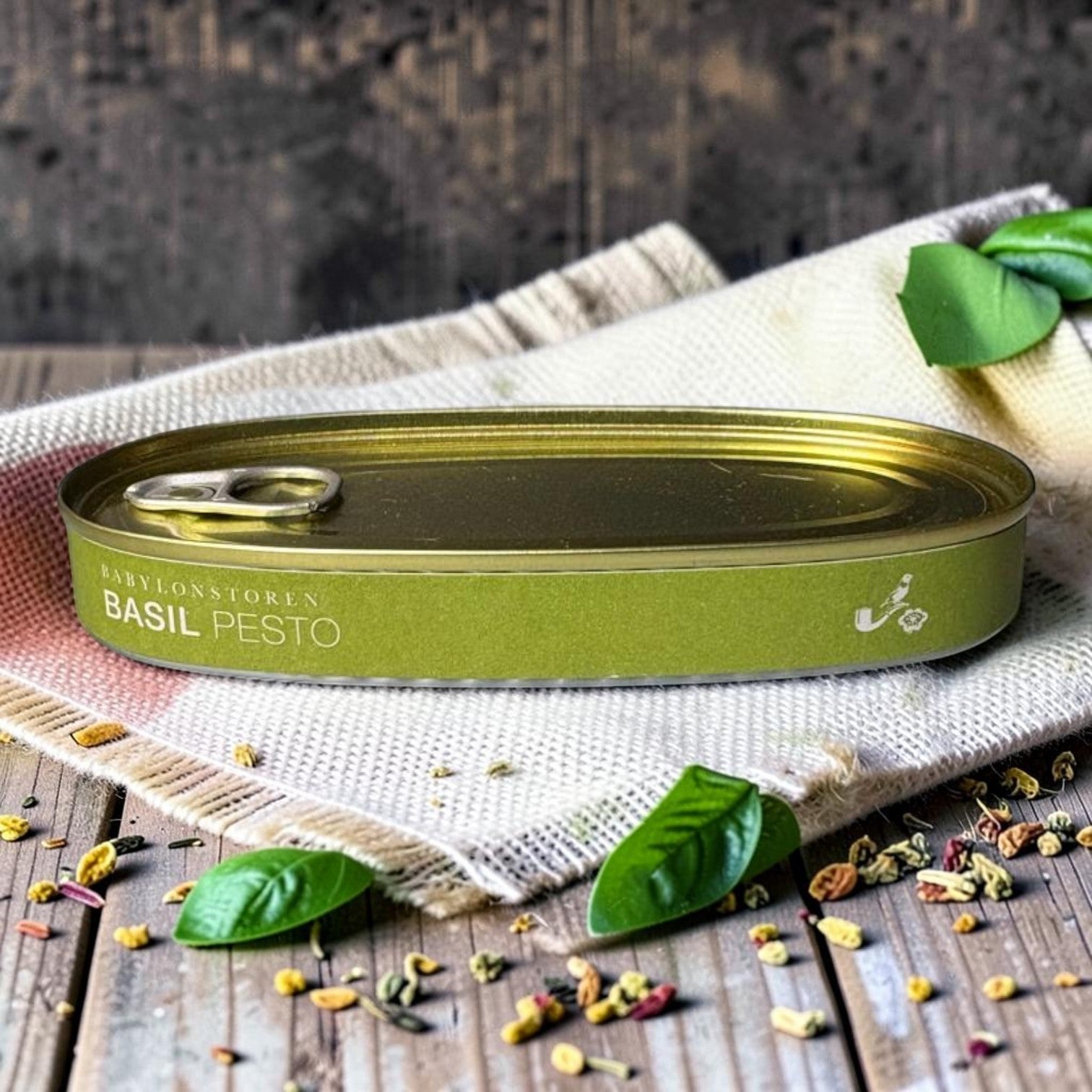 Die Spens Clarens Babylonstoren Basil Pesto in a green tin, garnished with fresh basil leaves and scattered spices.