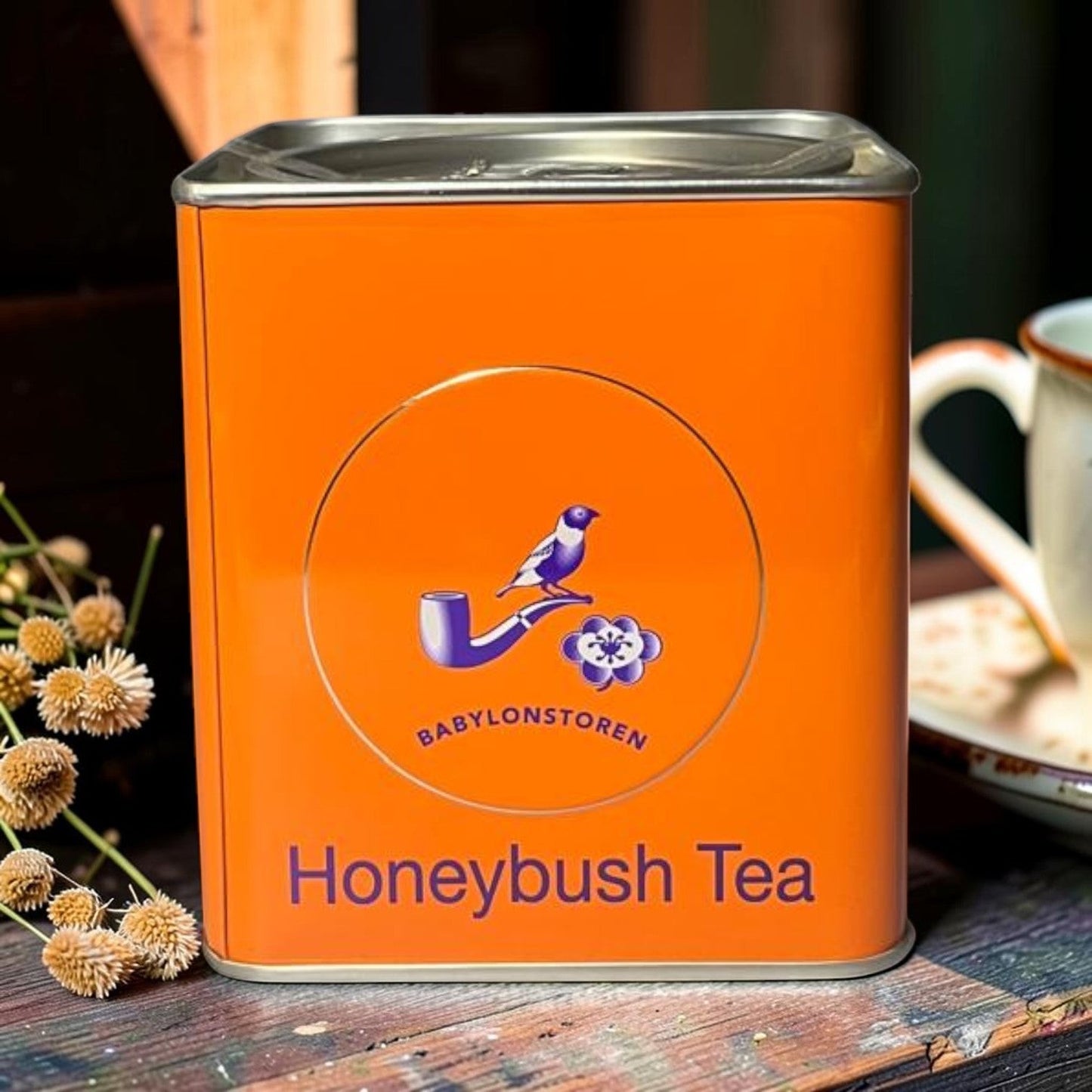 Die Spens Clarens Babylonstoren orange tin of caffeine-free Honeybush Tea, featuring a bird on a pipe and floral motif.