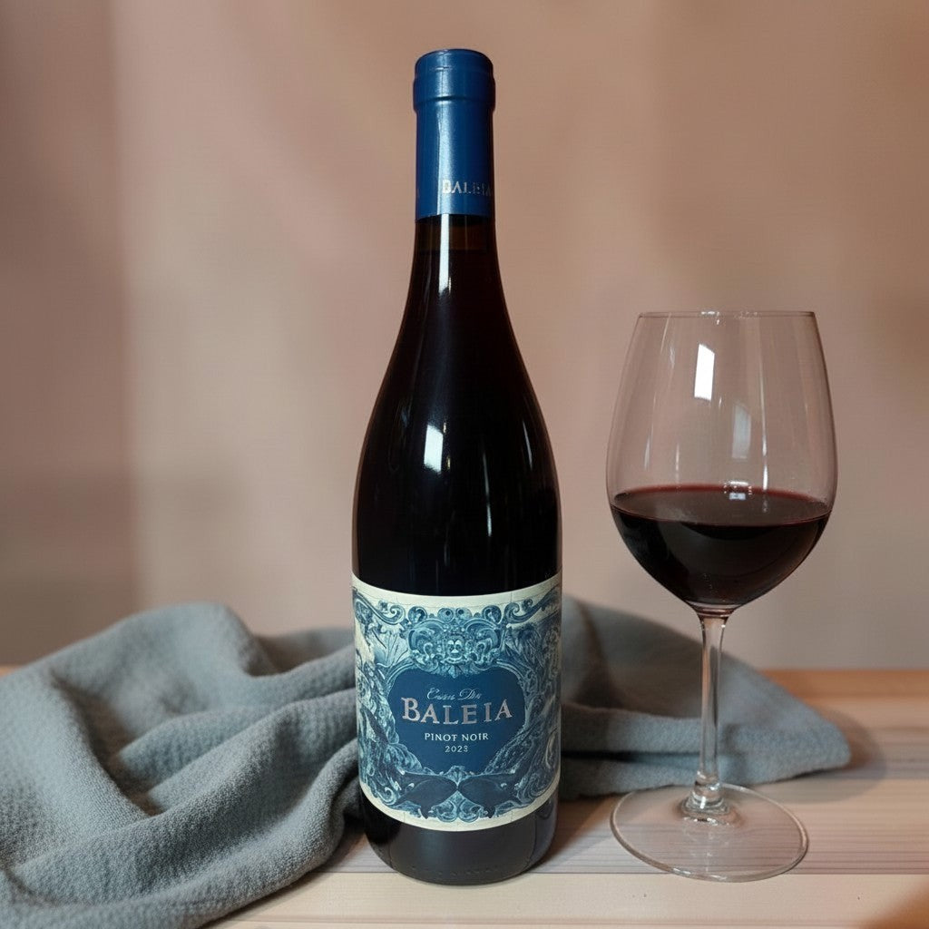 Die Spens Clarens Baleia Pinot Noir 2021 wine bottle and glass with red wine, grey cloth on wooden table.