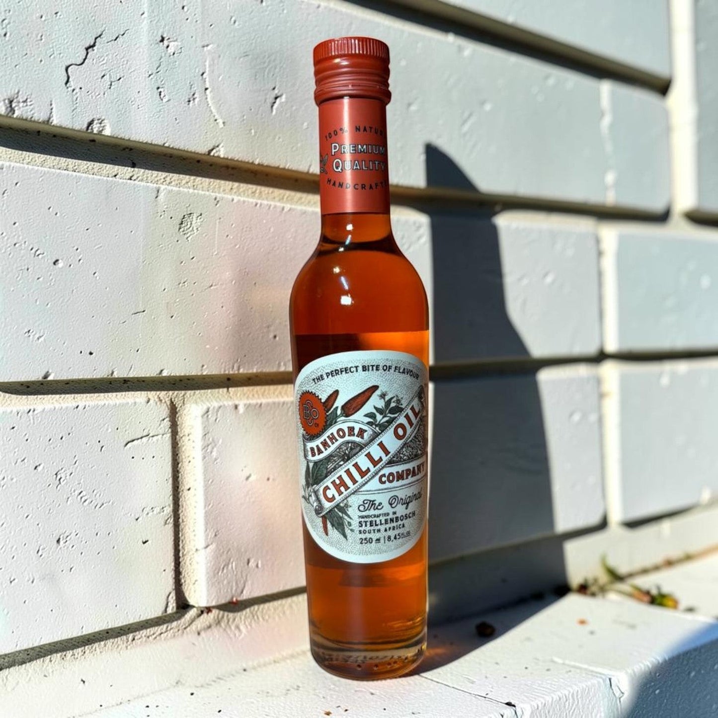Die Spens Clarens Banhoek Chilli Oil Original, a handcrafted, natural chilli oil with a rich amber hue in a clear glass bottle with a red cap.