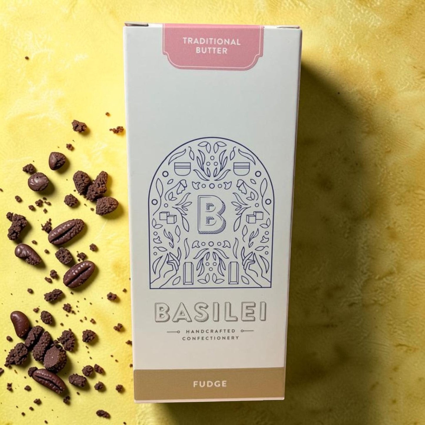 Die Spens Clarens Basilei Traditional Butter Fudge box with scattered fudge pieces on a yellow textured background.