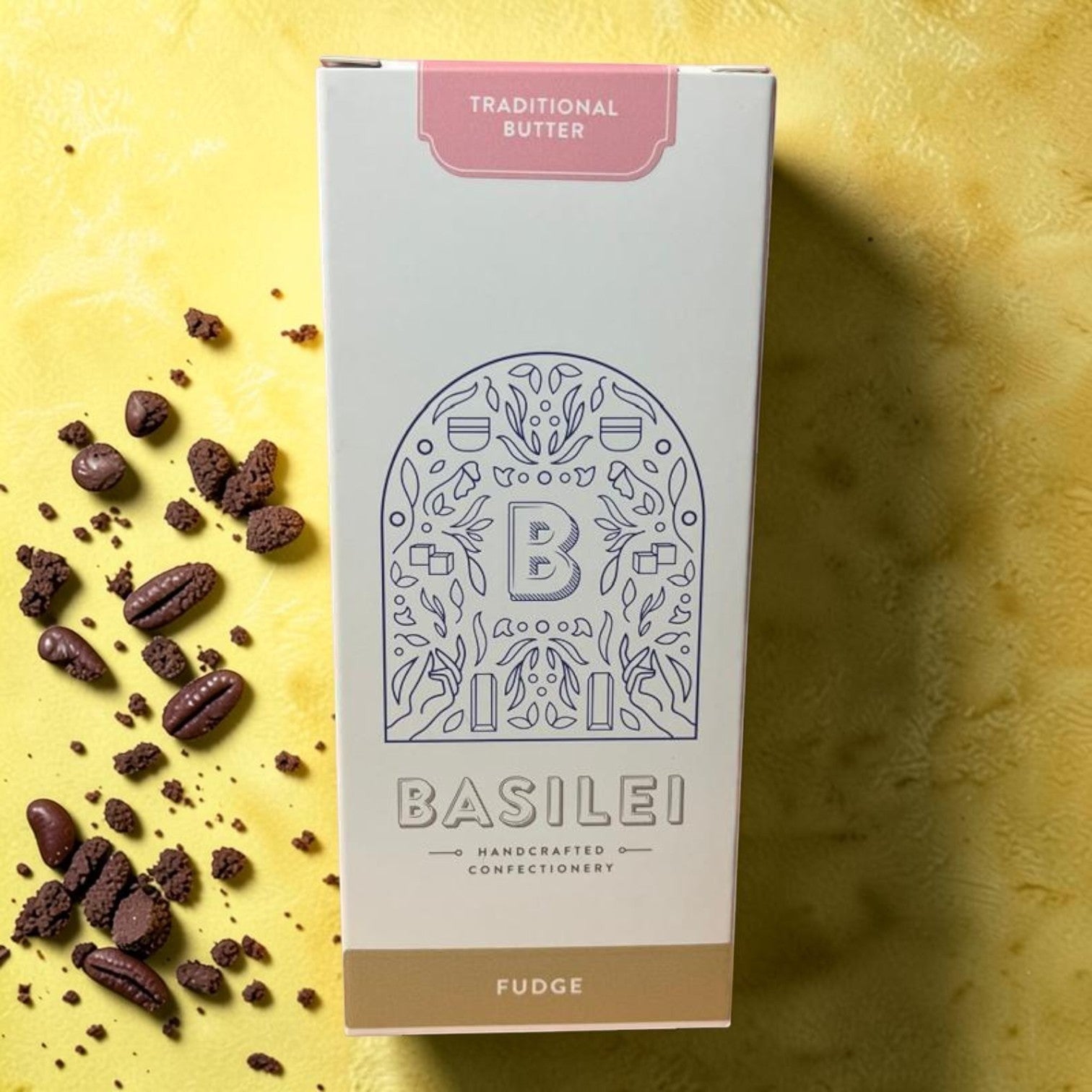Die Spens Clarens Basilei Traditional Butter Fudge box with scattered fudge pieces on a yellow textured background.
