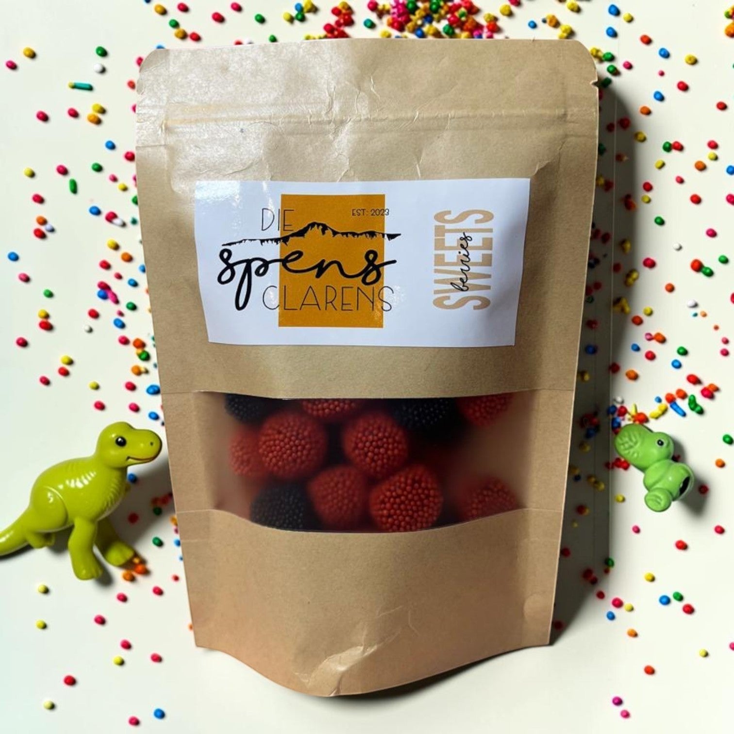 Die Spens Clarens bag of red and black berry-shaped gummy candies, surrounded by colorful sprinkles.