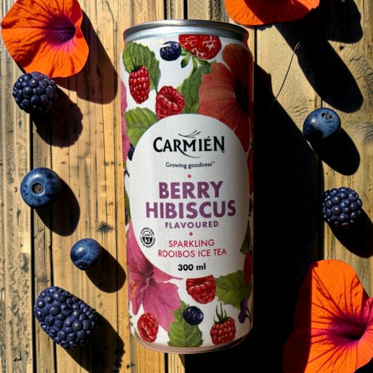 Die Spens Clarens Carmien Berry Hibiscus Sparkling Rooibos Ice Tea can surrounded by fresh berries and hibiscus flowers on a wooden surface.