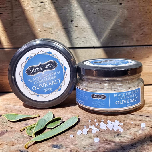 Die Spens Clarens African Salts Black Pepper & Coriander Olive Salt in a glass jar with loose salt crystals and leaves.