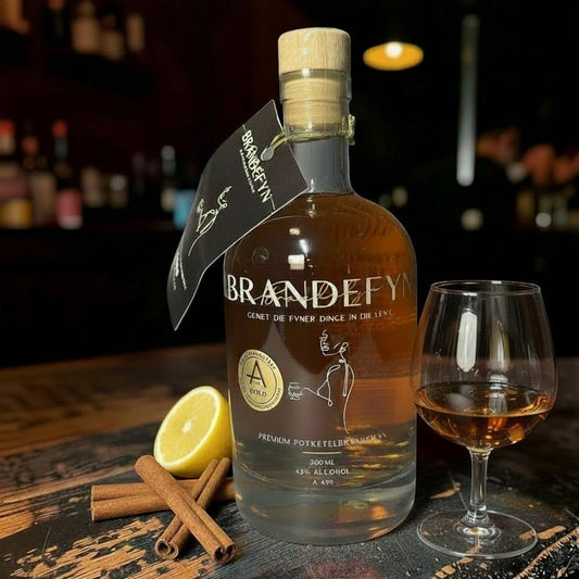 Die Spens Clarens Brandefyn premium potstill brandy in an elegant bottle with a glass, lemon, and cinnamon sticks.