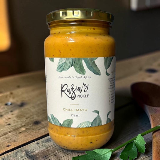 Die Spens Clarens Razia's Chilli Mayo in a glass jar with a gold lid, homemade in South Africa. Creamy orange condiment with visible chilli flakes.