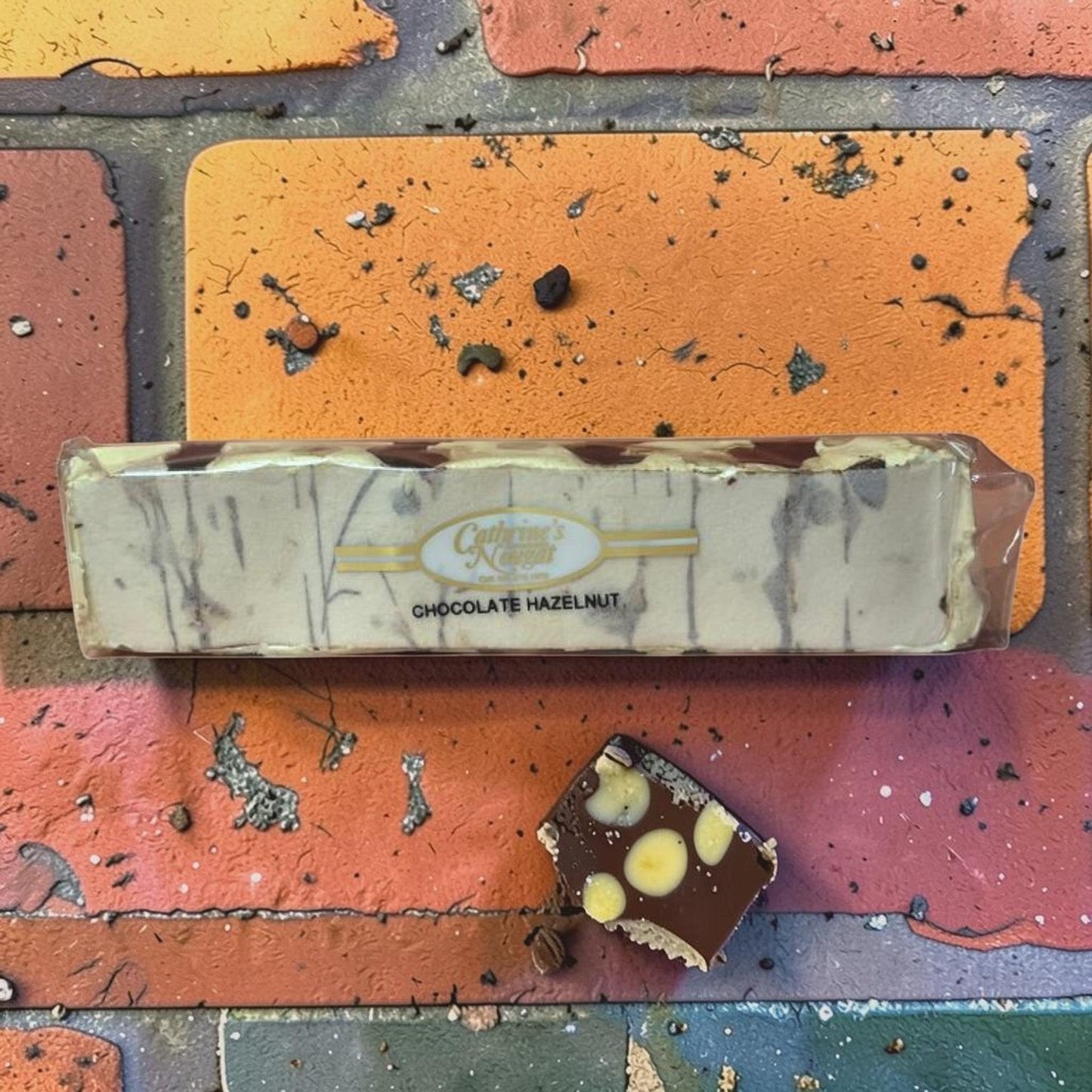 Die Spens Clarens Chocolate Hazelnut Nougat bar with swirls of chocolate and whole hazelnuts, with a sample piece showing chocolate, nougat, and hazelnuts.
