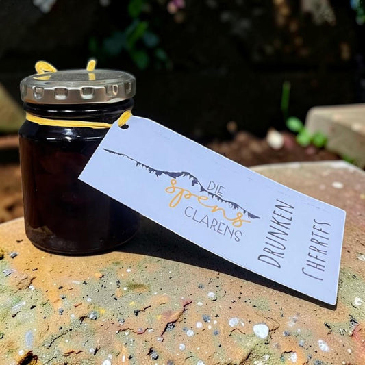 Die Spens Clarens Drunken Cherries in a glass jar with a yellow ribbon and a tag showing mountains and product name.