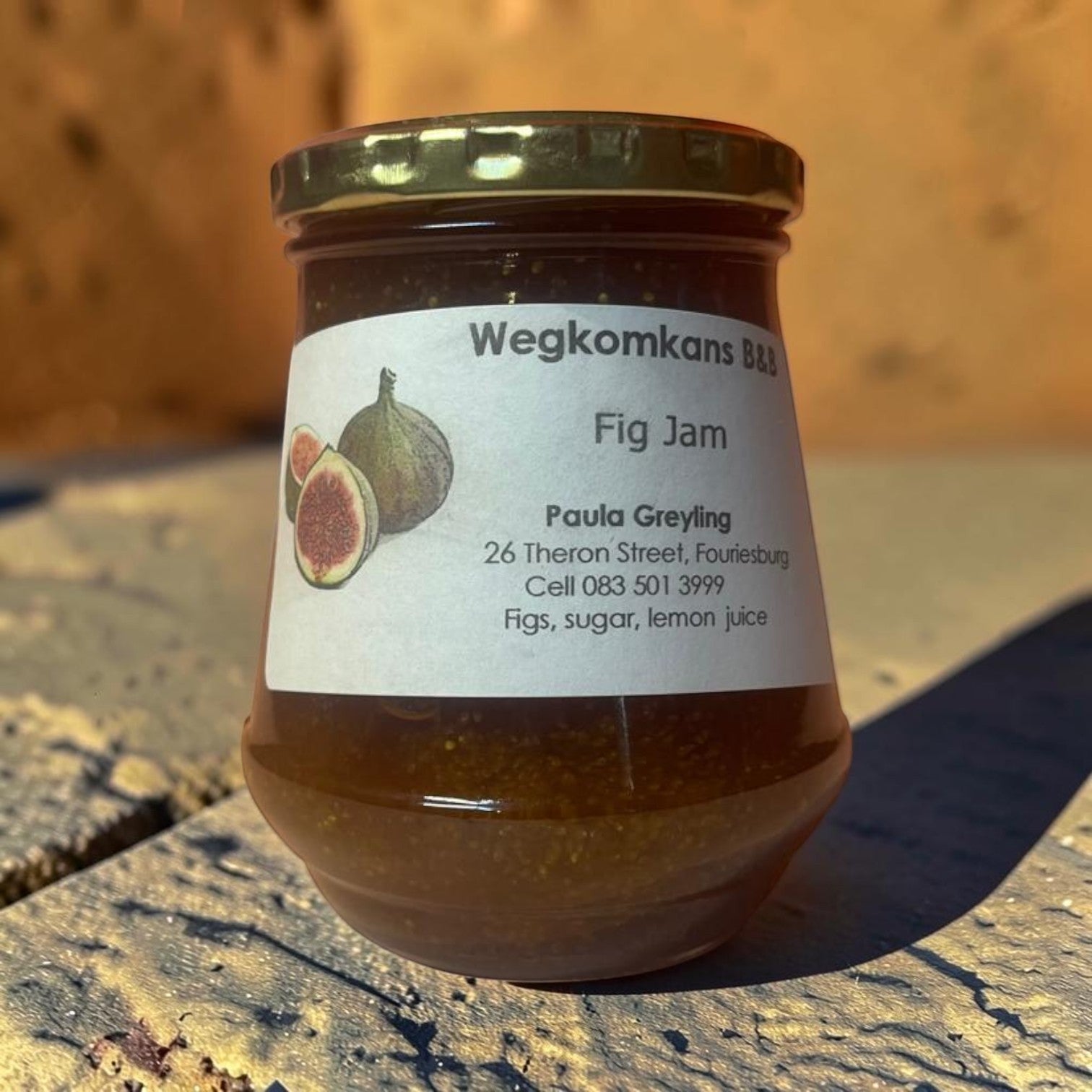 Die Spens Clarens Wegkomkans B&B fig jam in a glass jar with a gold lid. The label features illustrations of figs and lists ingredients.