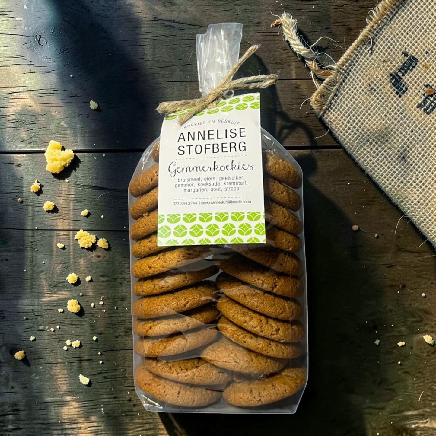 Die Spens Clarens Annelise Stofberg Gemmerkoekies traditional ginger cookies in a clear bag, stacked high on a wooden surface.