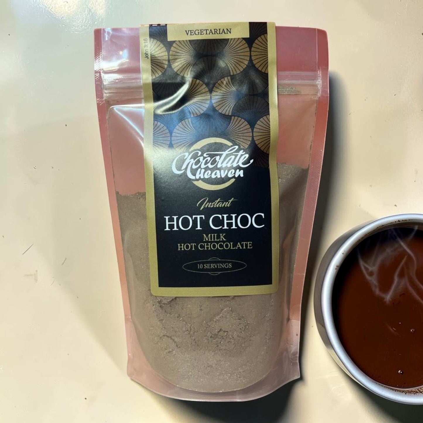 Die Spens Clarens Chocolate Heaven Instant Milk Hot Chocolate powder pouch next to a steaming mug of hot chocolate.