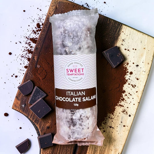 Die Spens Clarens Italian Chocolate Salami, a hand-crafted confection dusted with powdered sugar, on a wooden board with chocolate pieces.