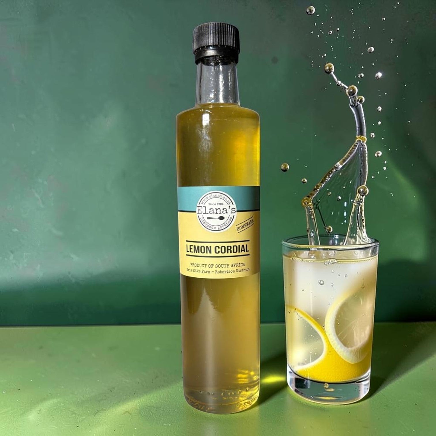 Die Spens Clarens Elana's Lemon Cordial bottle next to a glass of lemonade with lemon slices and a splash of liquid.