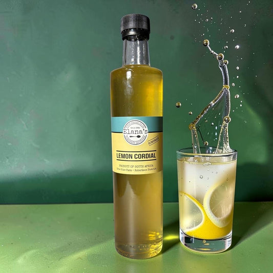 Die Spens Clarens Elana's Lemon Cordial bottle next to a glass of lemonade with lemon slices and a splash of liquid.