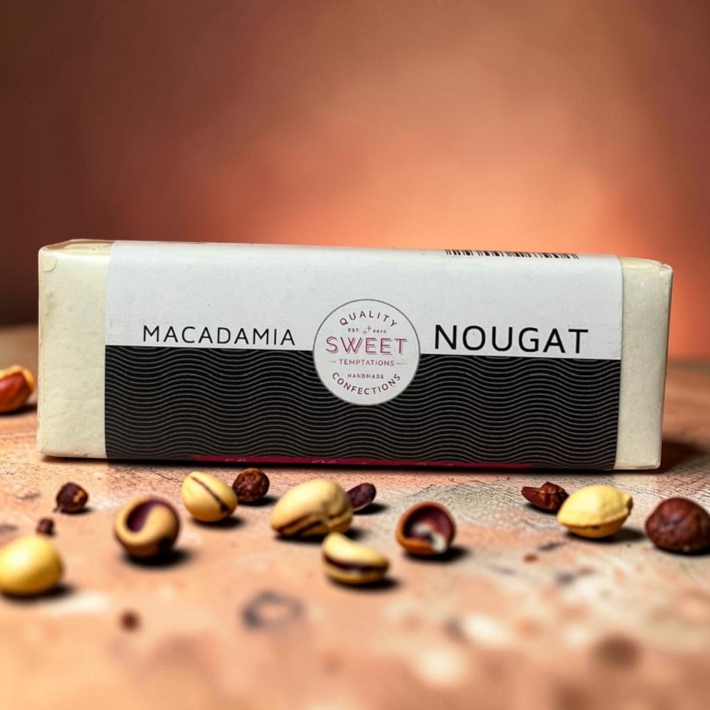 Die Spens Clarens Sweet Temptations Macadamia Nougat bar with macadamia nuts scattered around.