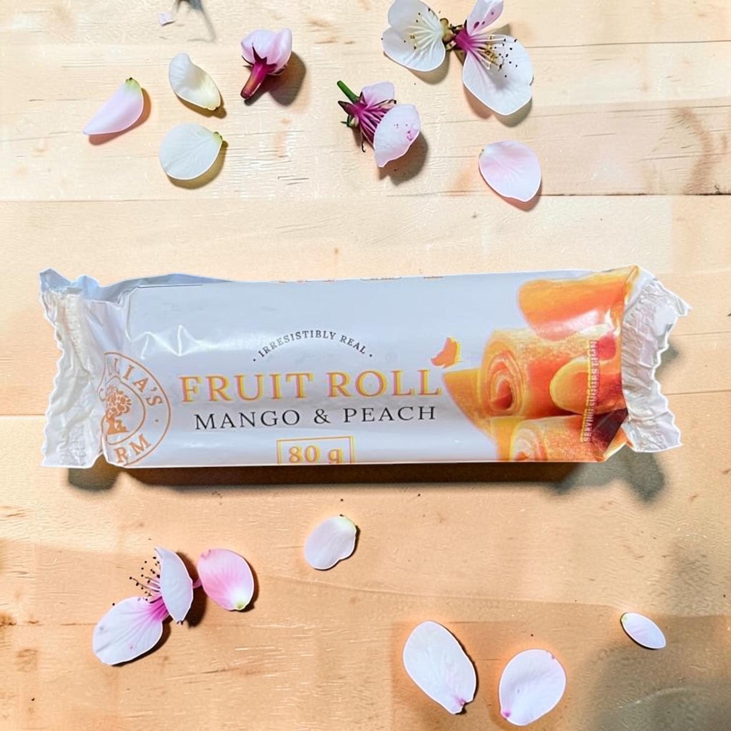 Die Spens Clarens Cecilias Farm Mango & Peach Fruit Roll packaging with fruit roll visible, surrounded by flower petals.