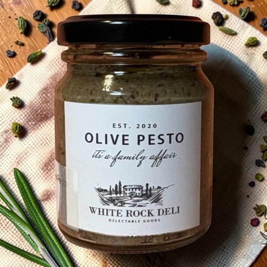 Die Spens Clarens White Rock Deli Olive Pesto in a glass jar with a black lid, garnished with rosemary and peppercorns.