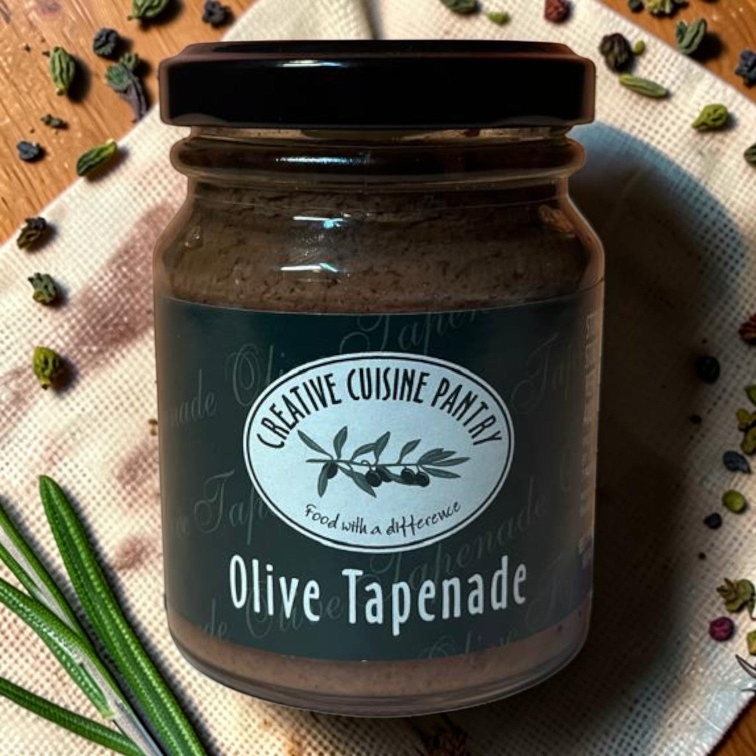 Die Spens Clarens Creative Cuisine Olive Tapenade in a glass jar with a black lid, featuring a label with olive branches.