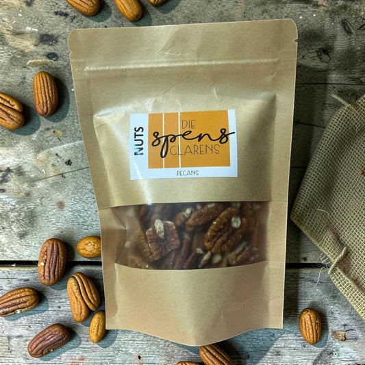 Die Spens Clarens resealable kraft bag filled with whole, rich pecan nuts. Scattered pecans on a wooden surface.