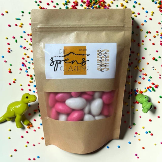 Die Spens Clarens pink and white candy-coated almonds in a brown resealable bag, surrounded by colorful sprinkles.
